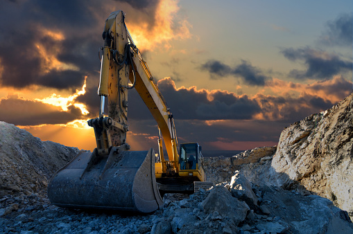 Image of a tracked excavator in a quarry with a setting sun and light rays Image of a tracked excavator in a quarry with a setting sun and light rays